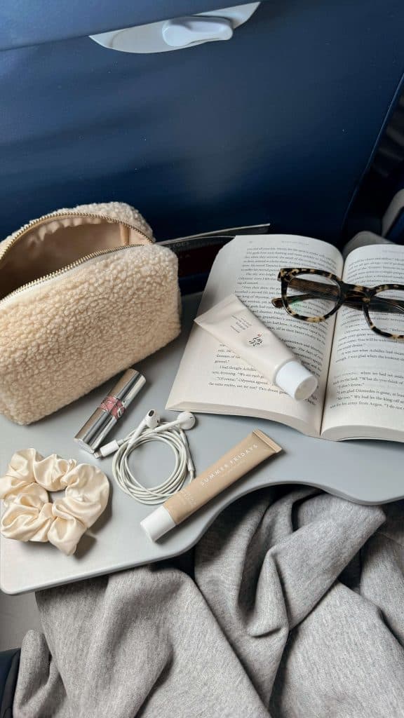 a cozy travel setup with a book, skincare products, and headphones on an airplane tray, showing healthy travel habits