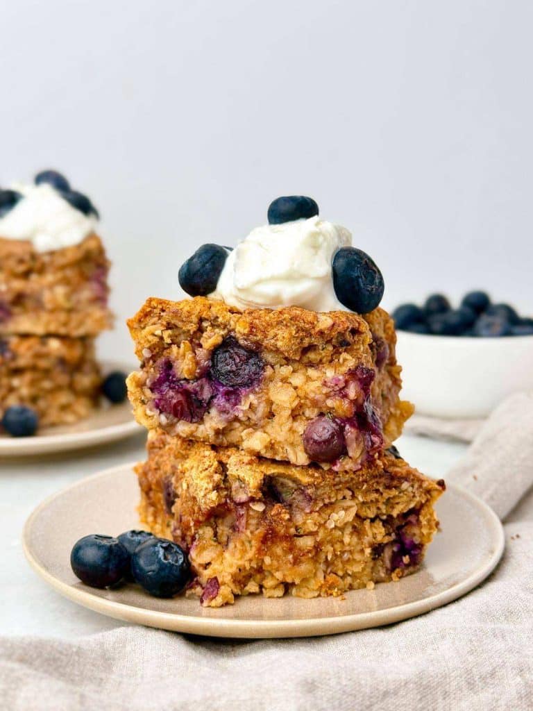 Blueberry baked oat bars stacked on a plate with whipped cream