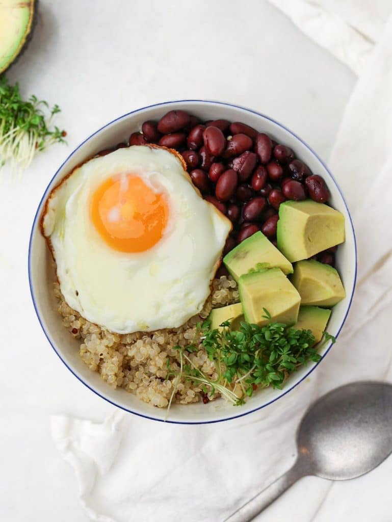 Quinoa breakfast bowl with fried egg, black beans, avocado, and microgreens