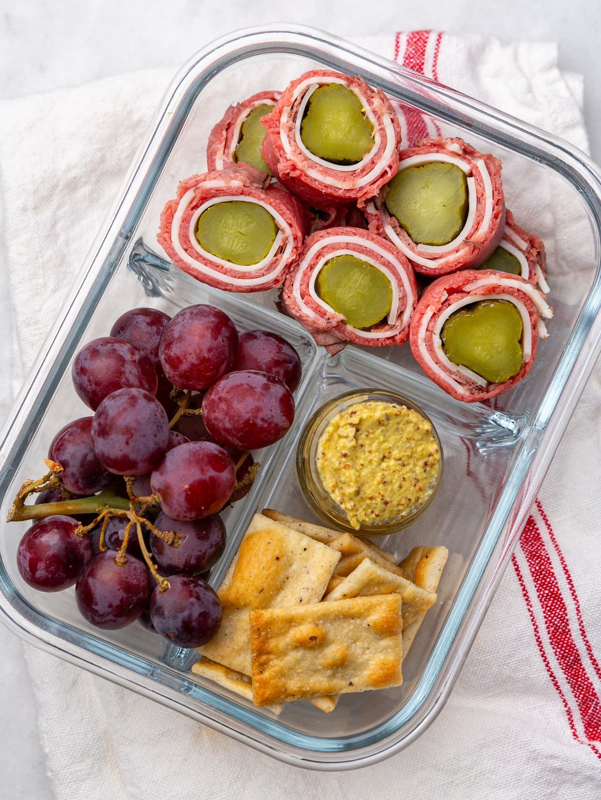 Roast beef and swiss roll-ups with pickles, grapes and mustard in a meal prep lunch box