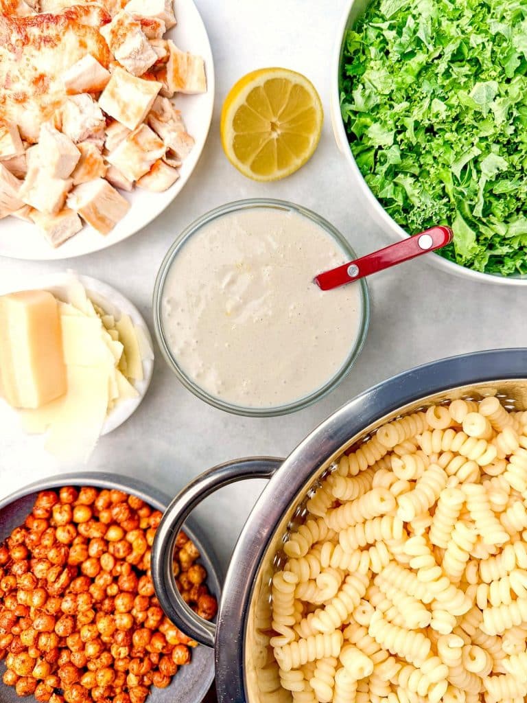 Kale pasta caesar salad ingredients flat lay with chicken, kale, dressing, and chickpeas
