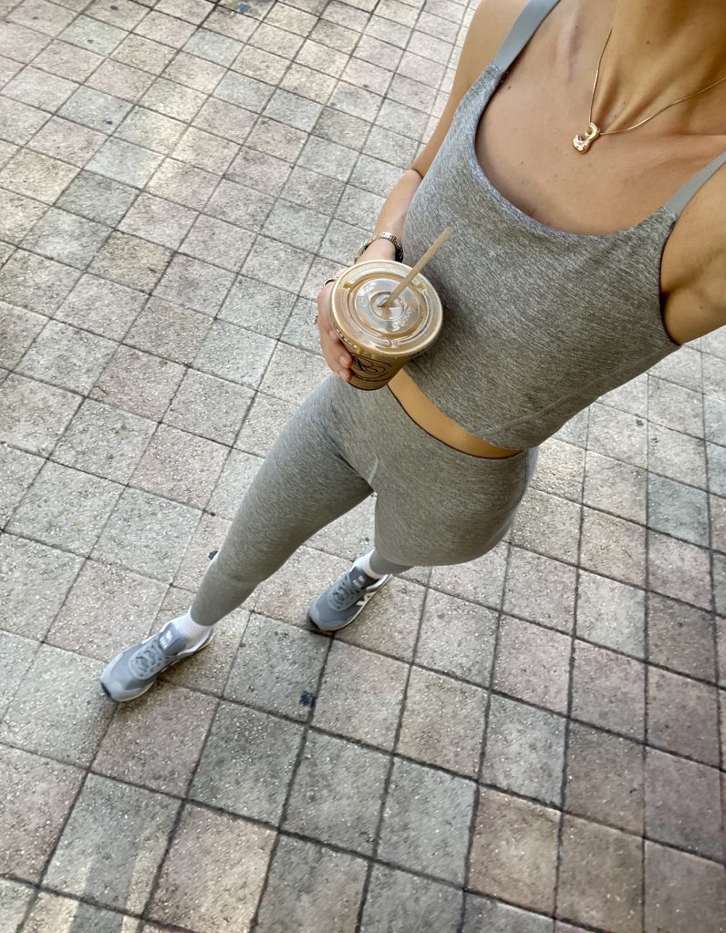a woman in athletic clothes on a walk with an iced coffee in hand