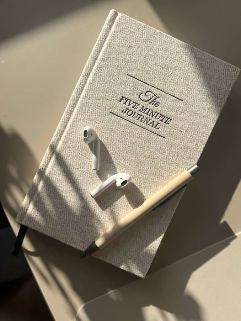 a beige gratitude journal with earphones and pen on a sunlit desk, representing mindful morning habits