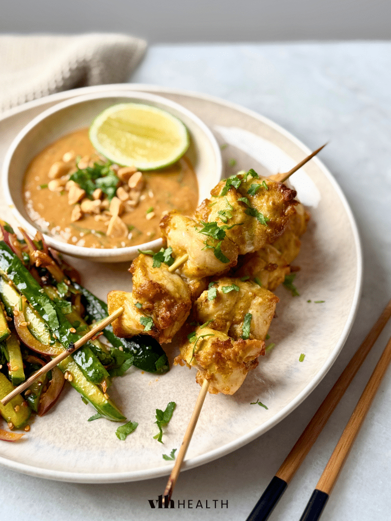 Juicy grilled chicken skewers served with a creamy peanut sauce, fresh lime, and stir-fried zucchini on a white plate. A flavorful and protein-packed low-carb dinner.