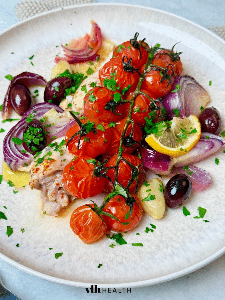 mediterranean sheet pan chicken with tomatoes, olives, and red onion.