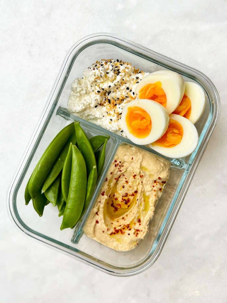 High protein lunch boxes with hard boiled eggs, everything bagel cottage cheese, hummus and snap peas