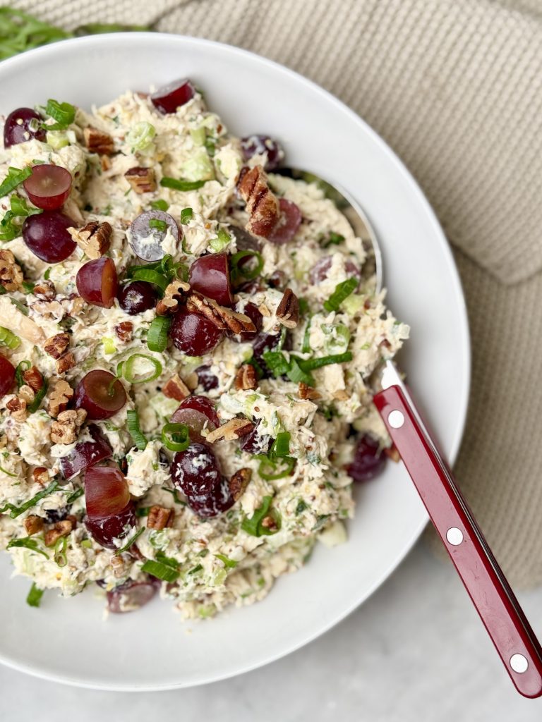 Creamy chicken salad with grapes, pecans, and fresh herbs in a white bowl, ready to be served.
