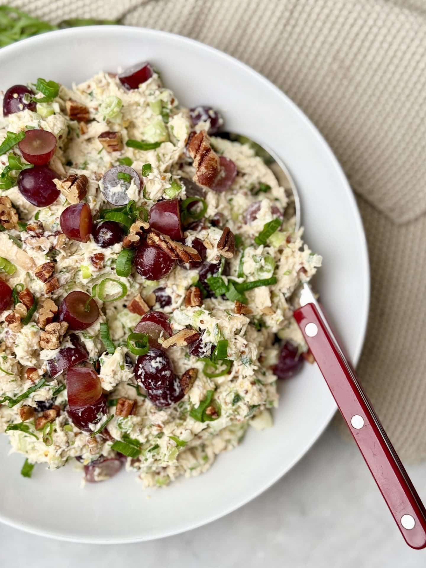 Creamy chicken salad with grapes, pecans, and fresh herbs in a white bowl, ready to be served.