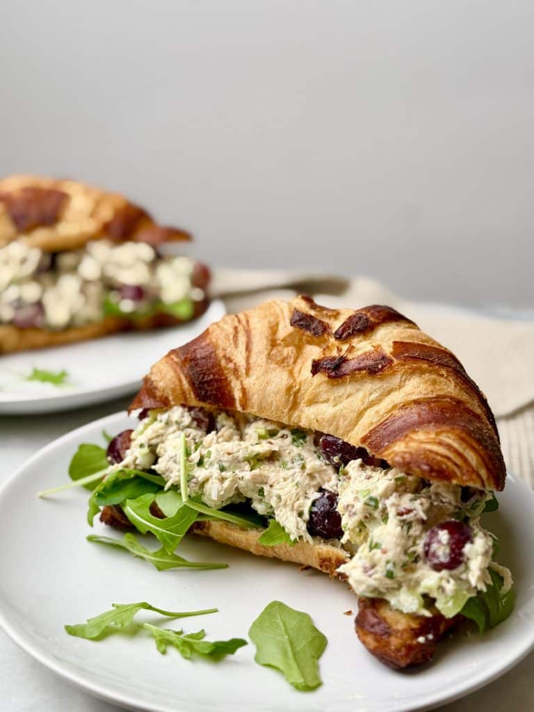 Close-up of a chicken salad croissant sandwich with grapes, showcasing the creamy texture and sweet grapes.
