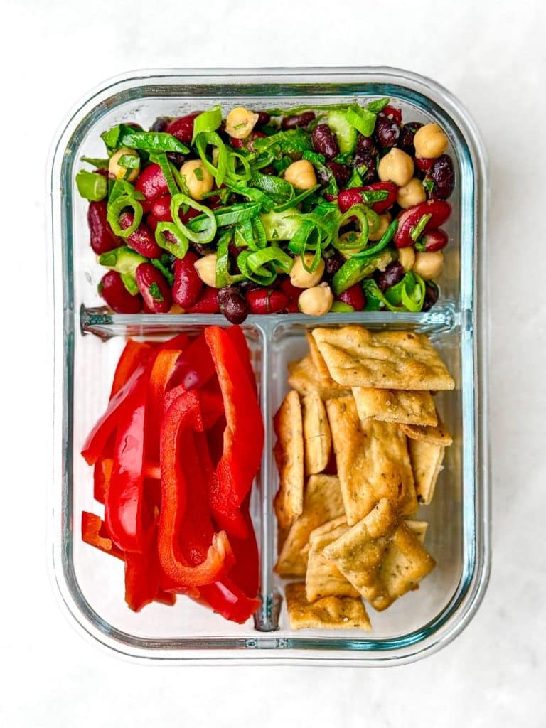 Simple black bean and kidney bean salad in a glass meal prep container with bell peppers and crackers
