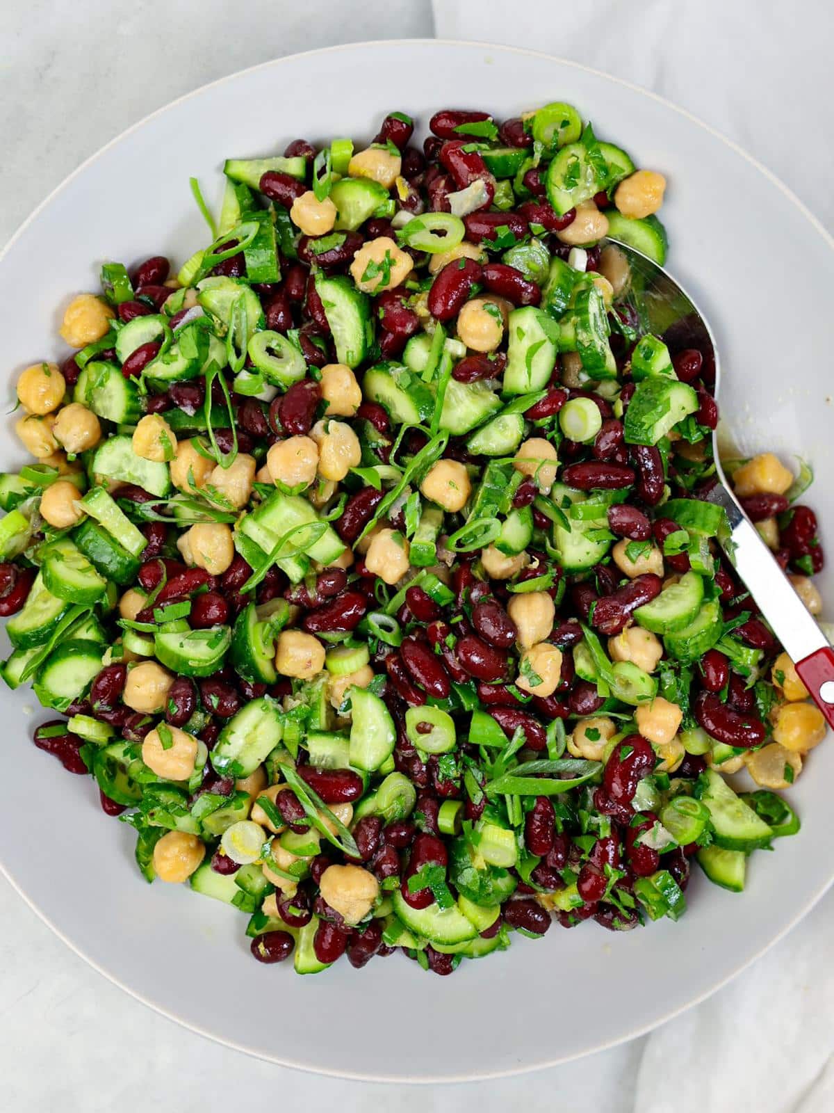 Simple kidney bean salad on a white plate with chickpeas, cucumber, parsley, and green onion