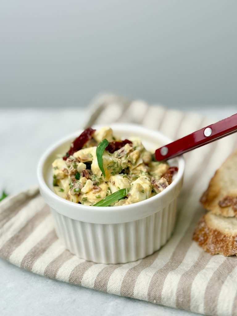 Creamy tarragon egg salad in a white ramekin with visible sun-dried tomatoes and fresh tarragon