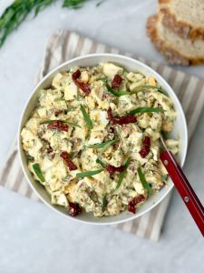 Bowl of egg salad with tarragon on striped towel, served with slices of sourdough bread