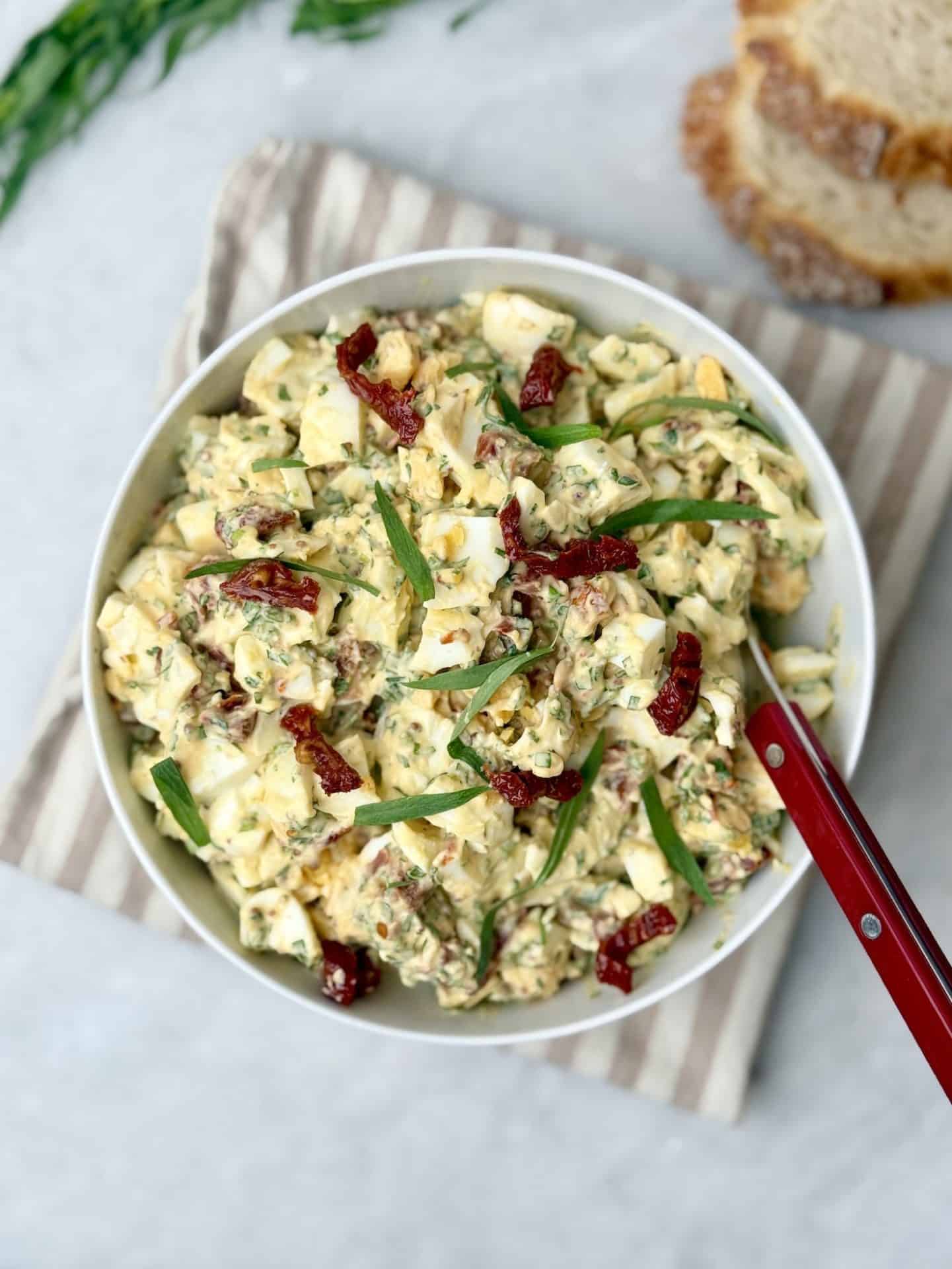 Bowl of egg salad with tarragon on striped towel, served with slices of sourdough bread