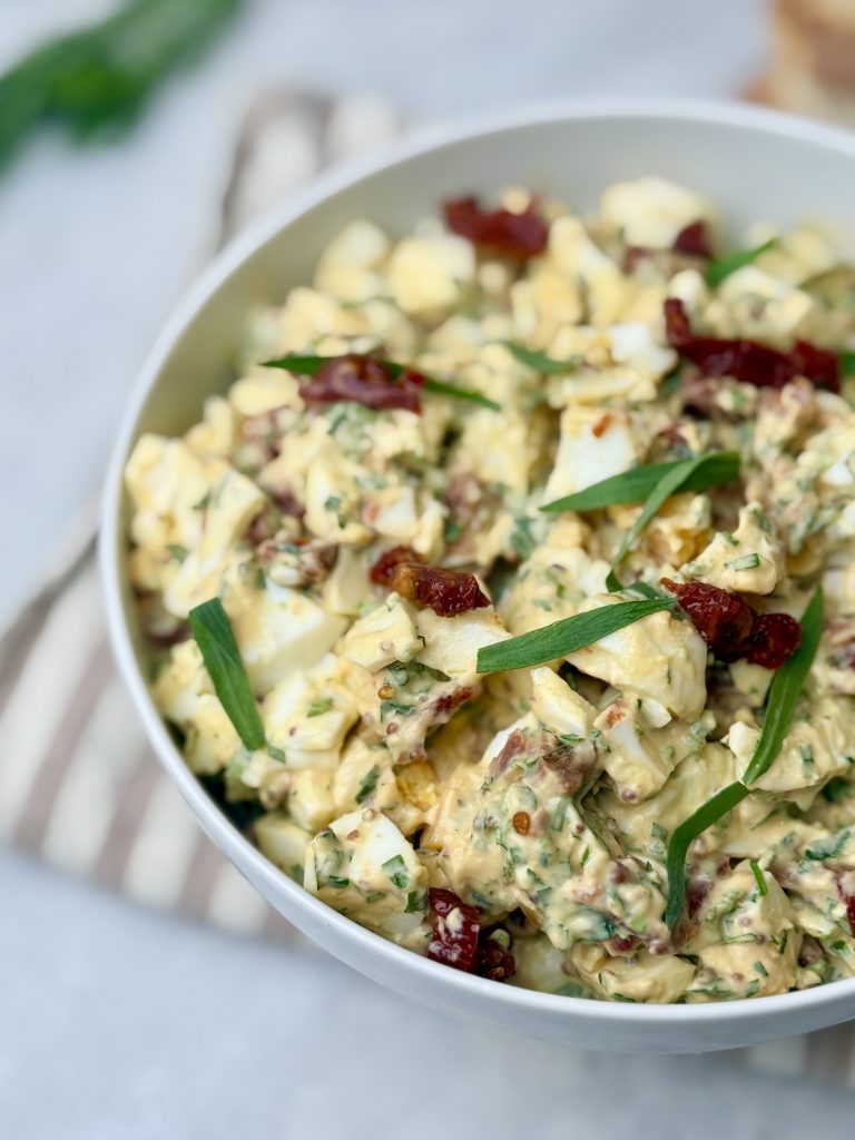 Close-up of tarragon egg salad showing chopped eggs, herbs, and sun-dried tomatoes
