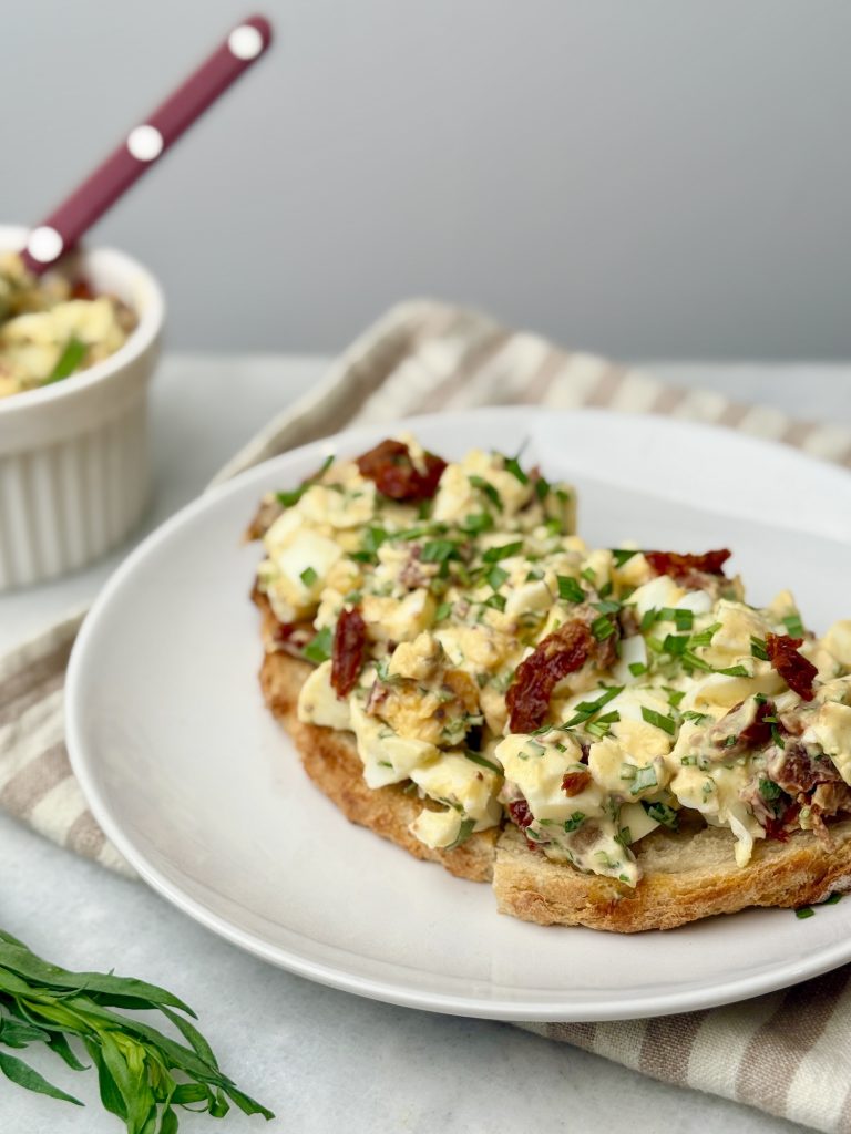 Open-faced tarragon egg salad on sourdough toast, topped with sun-dried tomatoes and fresh herbs