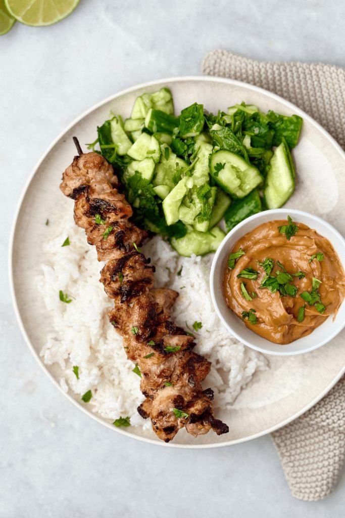Indonesian-style grilled chicken satay skewers over rice with creamy peanut sauce and cucumber herb salad — a flavorful main dish perfect for easy weeknight dinners or summer cookouts.
