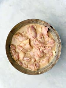 Boneless chicken thighs marinating in coconut milk, lime, garlic, and spices for Indonesian chicken satay.