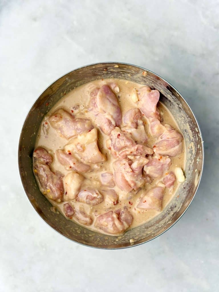 Boneless chicken thighs marinating in coconut milk, lime, garlic, and spices for Indonesian chicken satay.