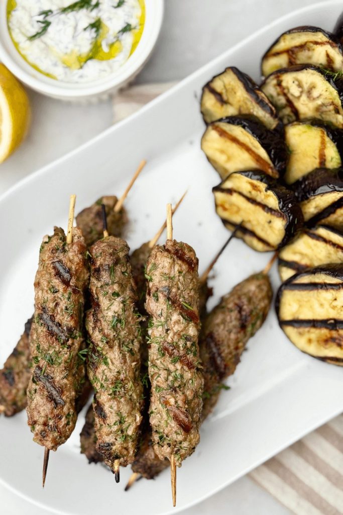 Middle Eastern lamb kofta skewers with tzatziki yogurt sauce and grilled eggplant slices — a bold and easy grilling recipe for your next summer BBQ or outdoor gathering.