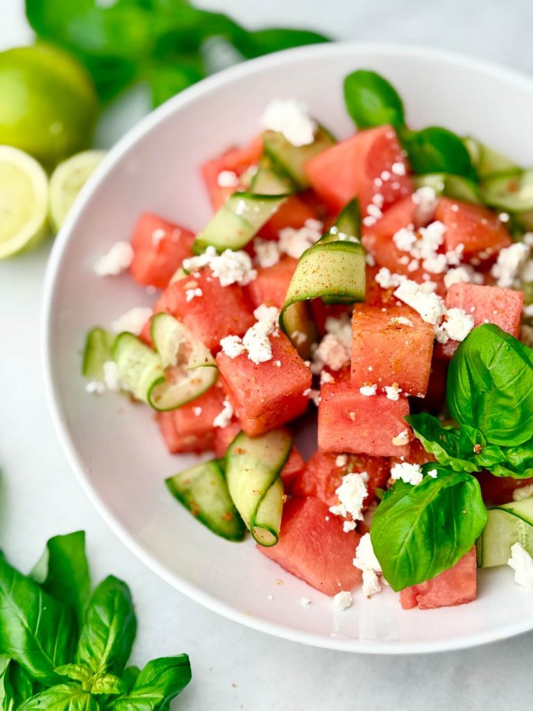 A vibrant bowl of Watermelon Feta Salad with Cucumber, fresh basil, and feta cheese styled on a marble background — perfect for summer.