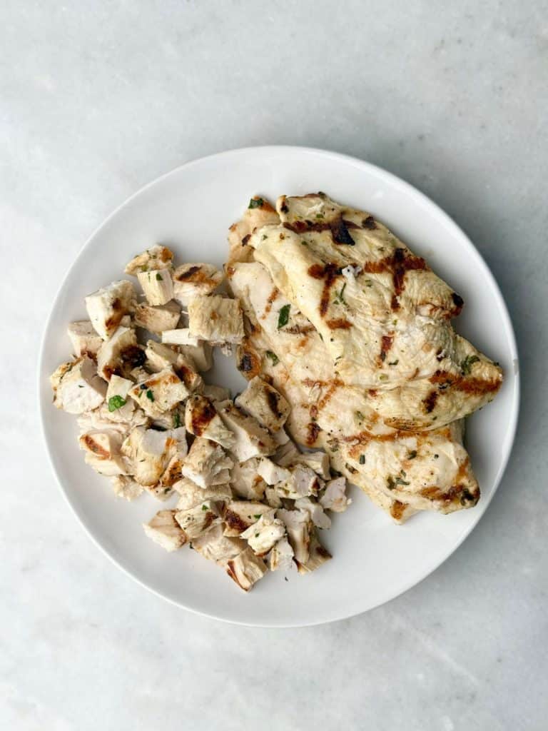 Grilled and chopped chicken on a white plate, golden brown and ready to be added to the Greek chicken and orzo pasta salad for added protein and flavor.