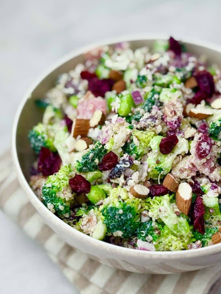 Close-up of creamy high protein broccoli salad with bacon, cranberries, almonds, and edamame in a white bowl, ideal for meal prep or summer lunch.