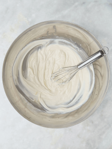 Creamy Greek yogurt-based dressing whisked in a metal bowl, used for a healthy high protein broccoli salad recipe.