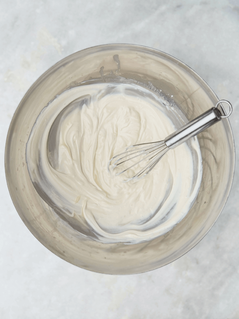 Creamy Greek yogurt-based dressing whisked in a metal bowl, used for a healthy high protein broccoli salad recipe.