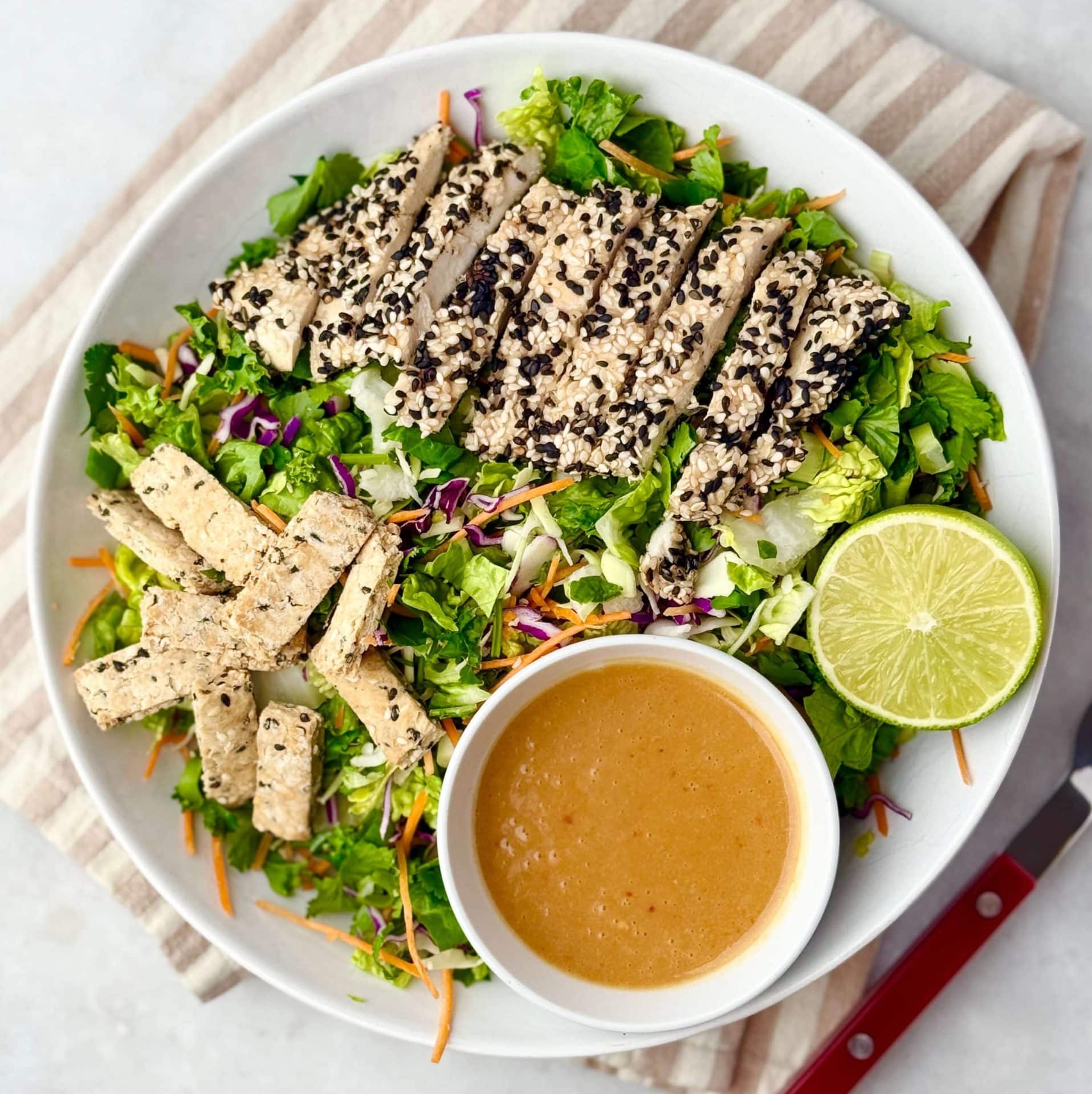 Bright top-down view of an Erewhon Asian Chicken Salad with sliced chicken breast, shredded greens, and a lime wedge beside the miso-ginger dressing.