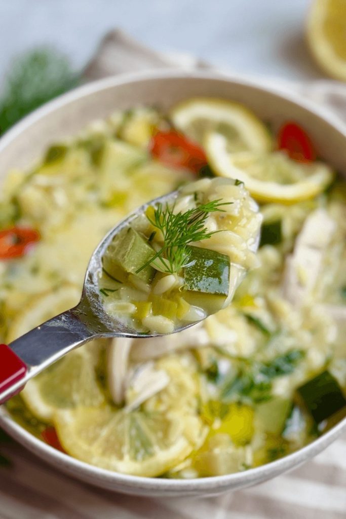 Spoonful of Greek avgolemono-inspired chicken soup with zucchini, lemon slices, and orzo pasta — light and packed with protein.