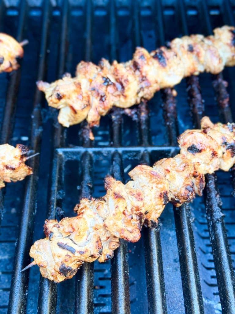 Marinated chicken skewers sizzling on a gas grill for authentic Indonesian chicken satay with charred edges.