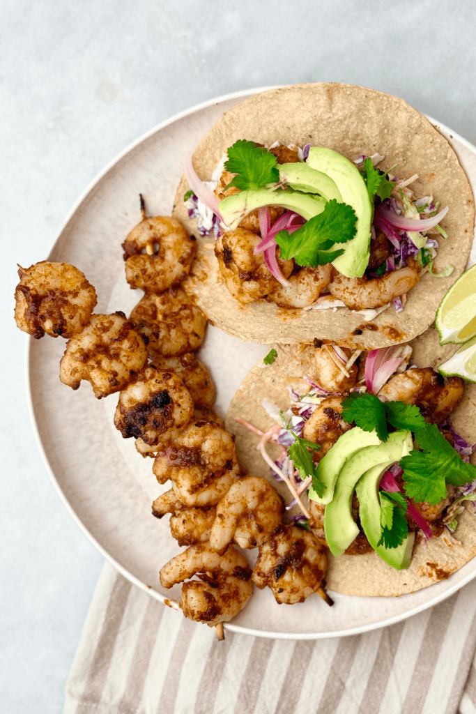 two grilled shrimp tacos topped with avocado and cilantro