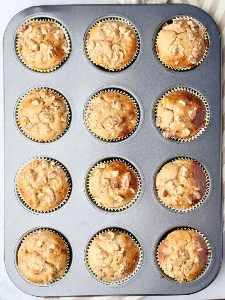 Overhead view of high protein banana bread muffins baked in a muffin pan with golden tops and chopped walnuts.