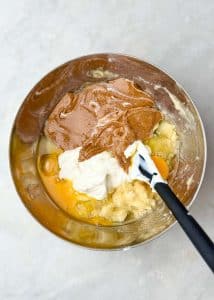 Mixing bowl filled with mashed banana, whole eggs, almond butter, and Greek yogurt for banana bread protein muffins.