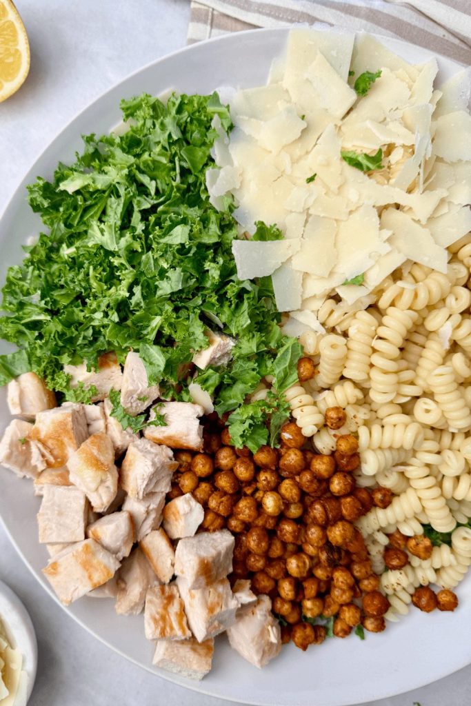 Kale Caesar salad with grilled chicken, roasted chickpeas, Parmesan, and pasta — a creative high protein low calorie lunch idea.