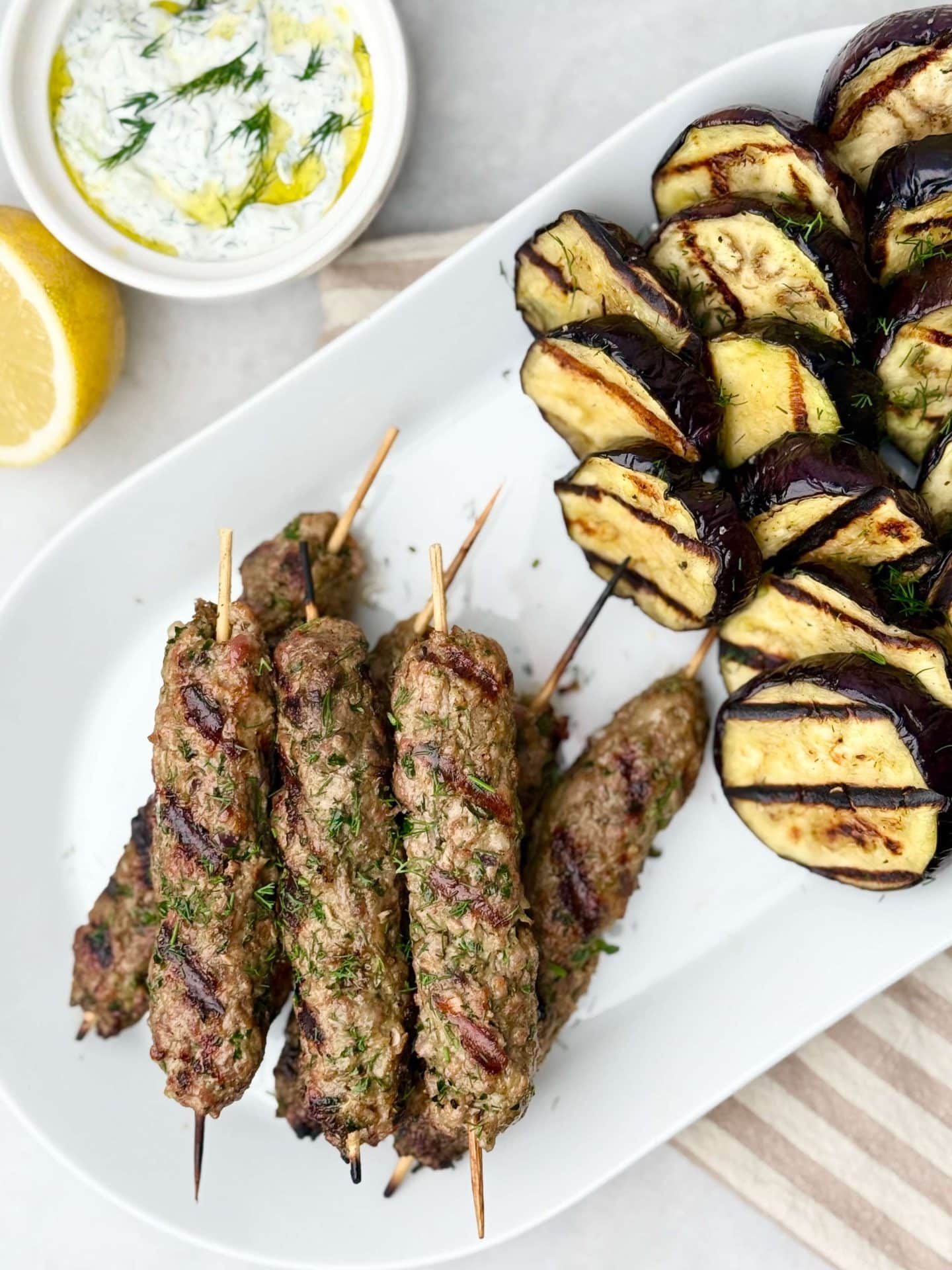 Grilled lamb kofta and tzatziki served with smoky eggplant rounds, fresh dill, and lemon for a bold and healthy summer dinner.