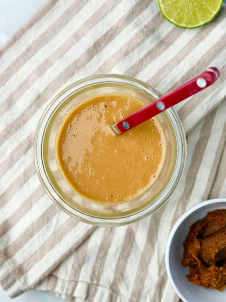 Homemade miso-ginger dressing in a jar with a red spoon, part of the signature Erewhon Asian Chicken Salad recipe.