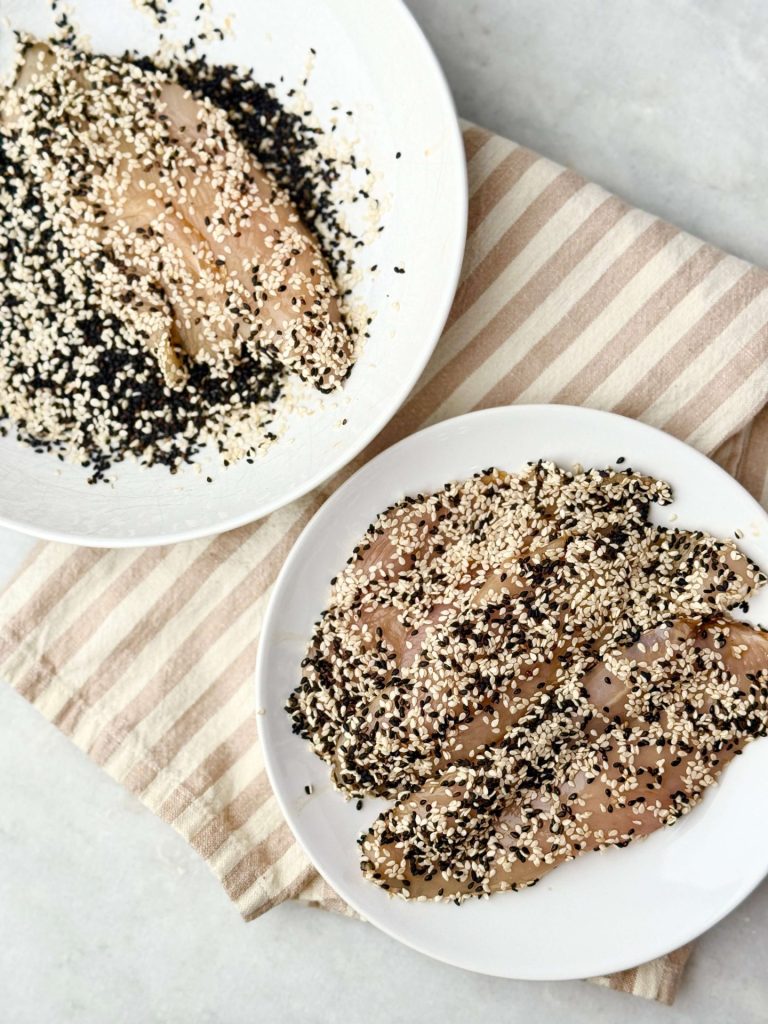 Raw chicken cutlets coated in black and white sesame seeds.