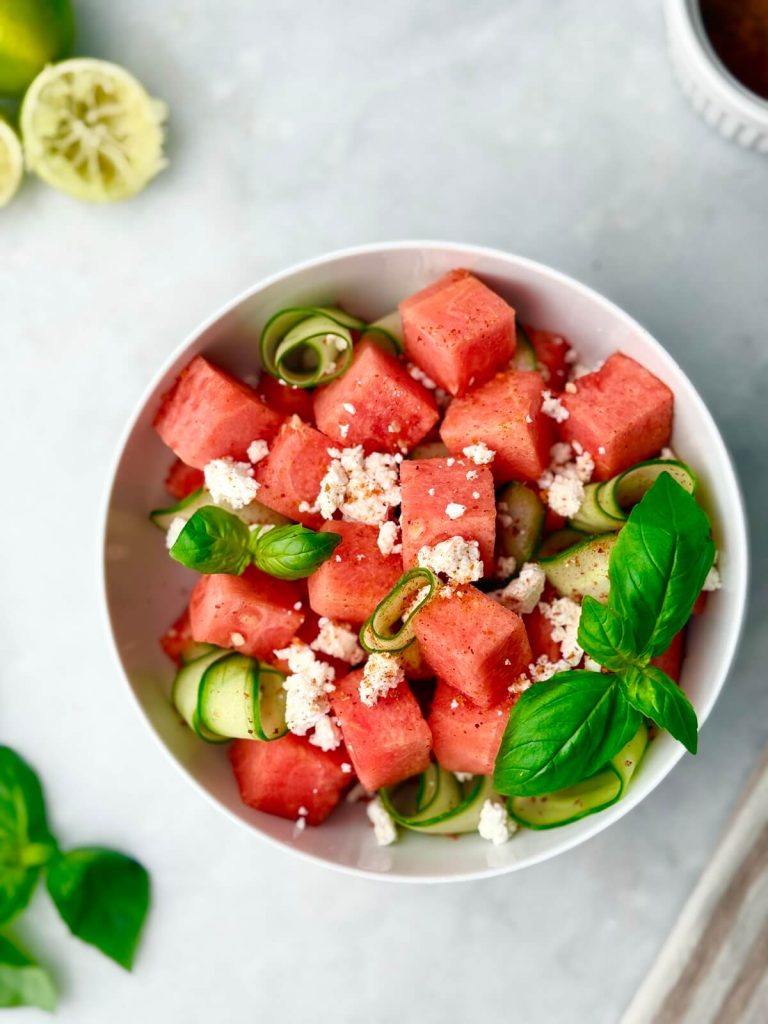 Overhead photo of a simple summer salad with watermelon, cucumber, and feta, styled with a striped linen napkin.
