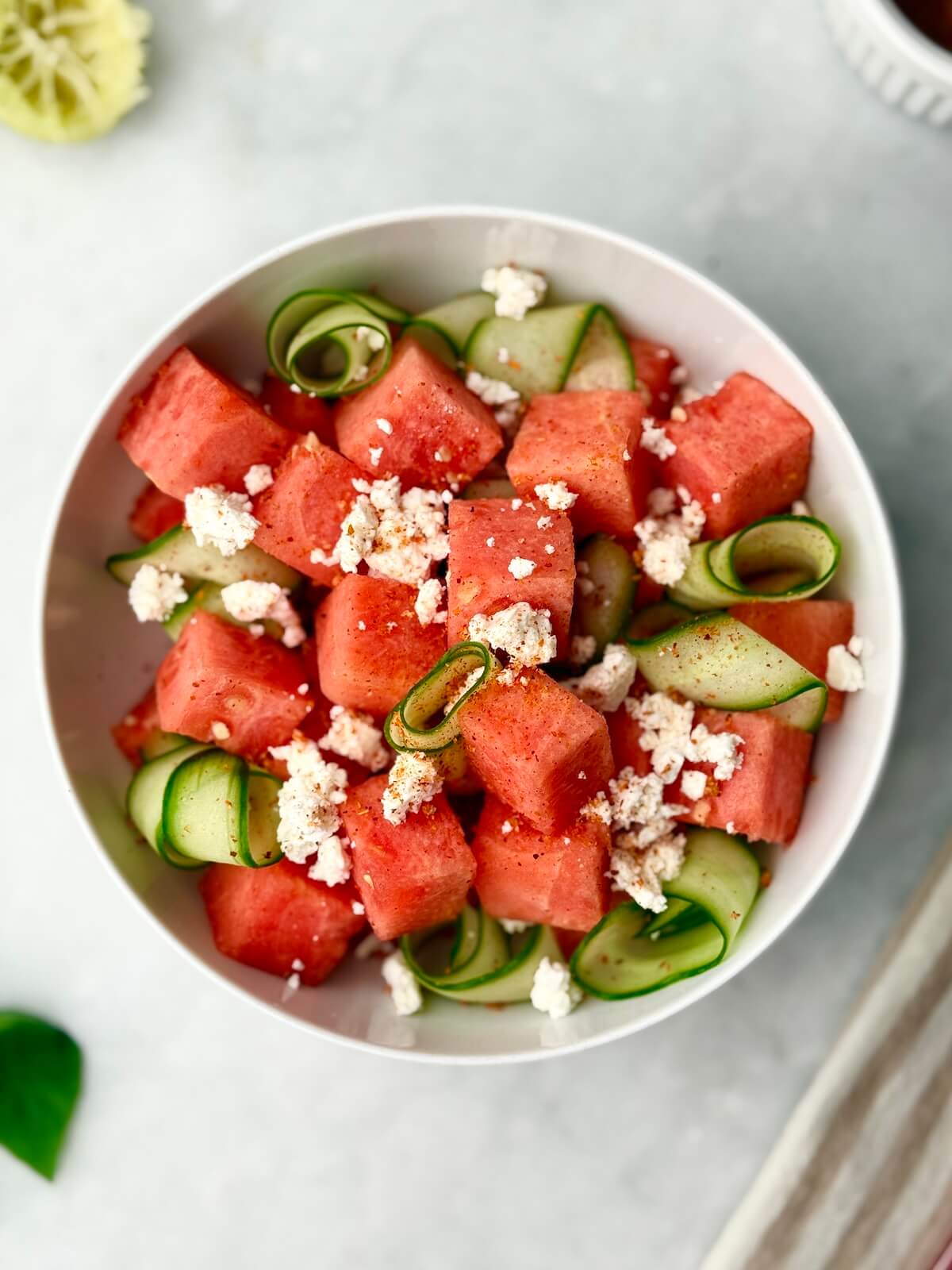 Close-up view of juicy watermelon cubes, crisp cucumber ribbons, tangy feta, and fresh basil in a refreshing summer salad.