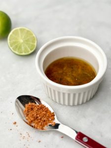 Homemade chili-lime vinaigrette and seasoning displayed with a spoon and ramekin, perfect for drizzling over Watermelon Feta Salad with Cucumber.