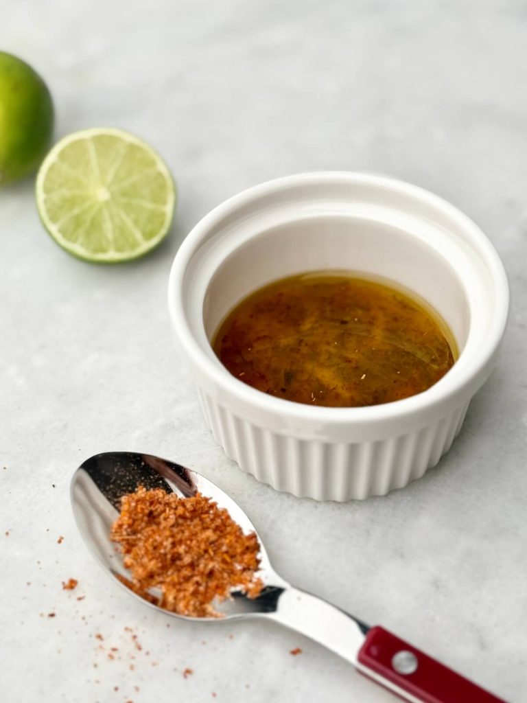 Homemade chili-lime vinaigrette and seasoning displayed with a spoon and ramekin, perfect for drizzling over Watermelon Feta Salad with Cucumber.
