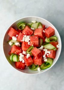 Watermelon Feta Salad with Cucumber in progress — fresh watermelon cubes mixed with cucumber ribbons and crumbled feta in a white bowl.
