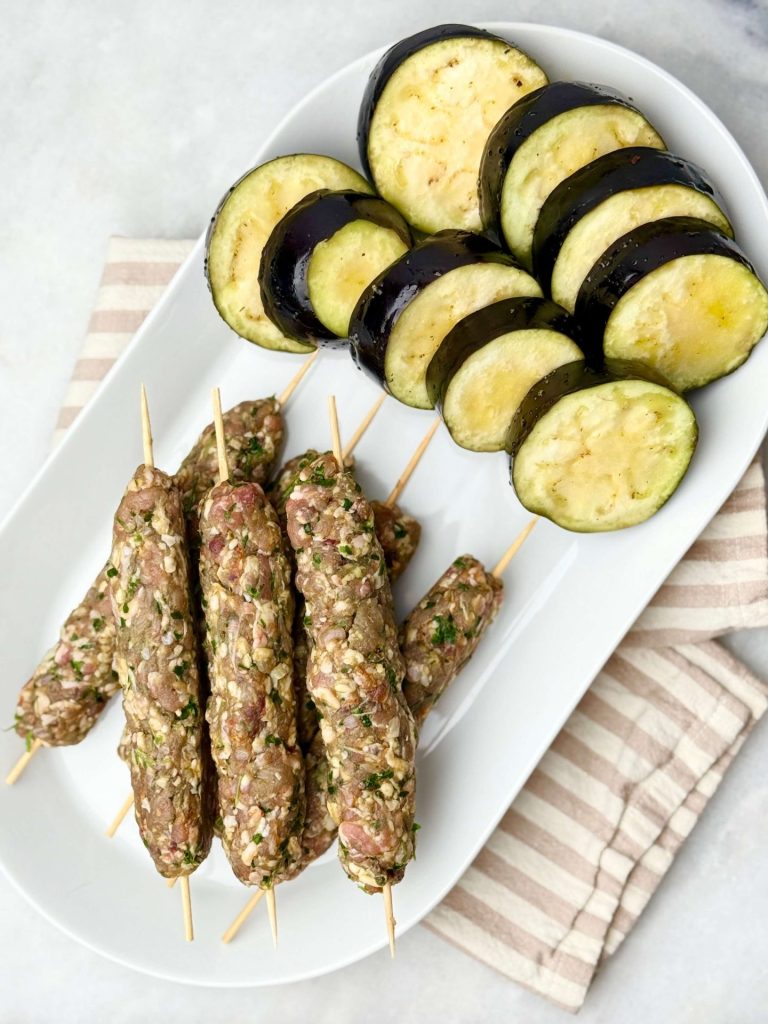 Uncooked lamb kofta skewers and sliced eggplant prepared for grilling, a fresh step in the lamb kofta and tzatziki recipe.