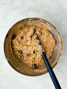 Mixing bowl of high protein blueberry breakfast cookie dough. Thick batter made with almond butter, coconut flakes, collagen, and blueberries.