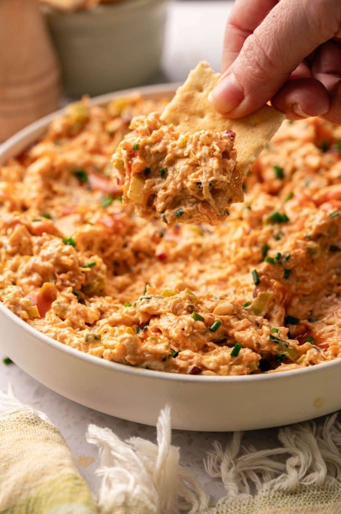 Hand holding a pita chip scooped with buffalo chicken salad.