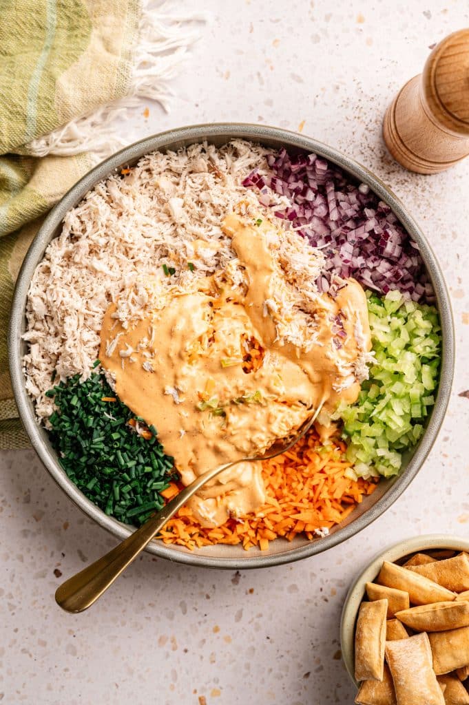 Spoon stirring buffalo dressing into shredded chicken and vegetables.