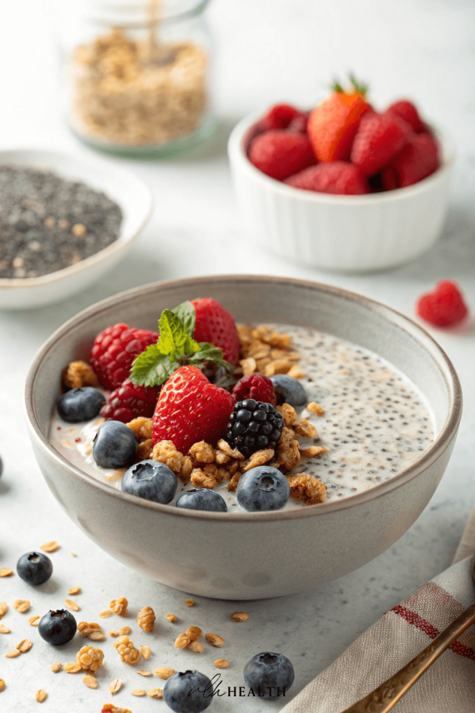 Bowl of chia seed pudding topped with fresh raspberries, blueberries, blackberries, crunchy granola, and a mint garnish on a white surface.