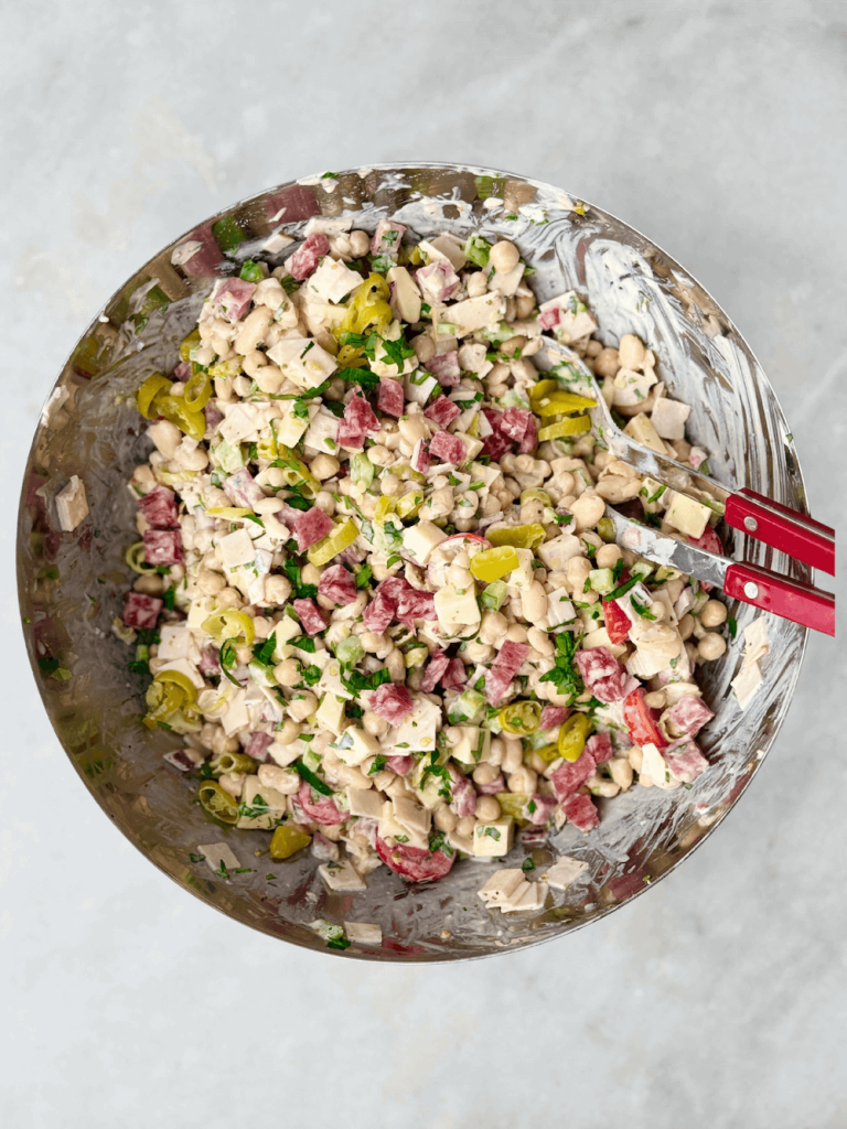 Italian grinder bean salad fully mixed in a stainless steel bowl coated with creamy dressing and garnished with fresh herbs.
